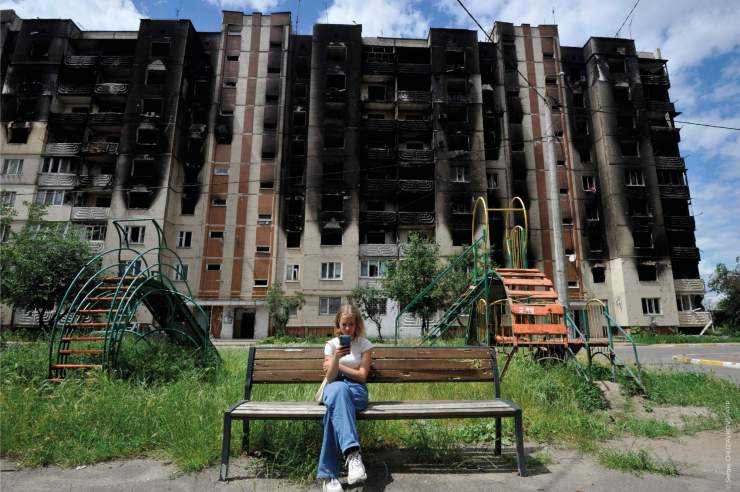 Une jeune fille regarde son smartphone, assise sur un banc devant des immeubles résidentiels partiellement détruits à la suite du bombardement de la ville d’Irpin, près de la capitale ukrainienne, Kyiv, le 16 juin 2022, alors que la guerre russo-ukrainienne entre dans son 113e jour.